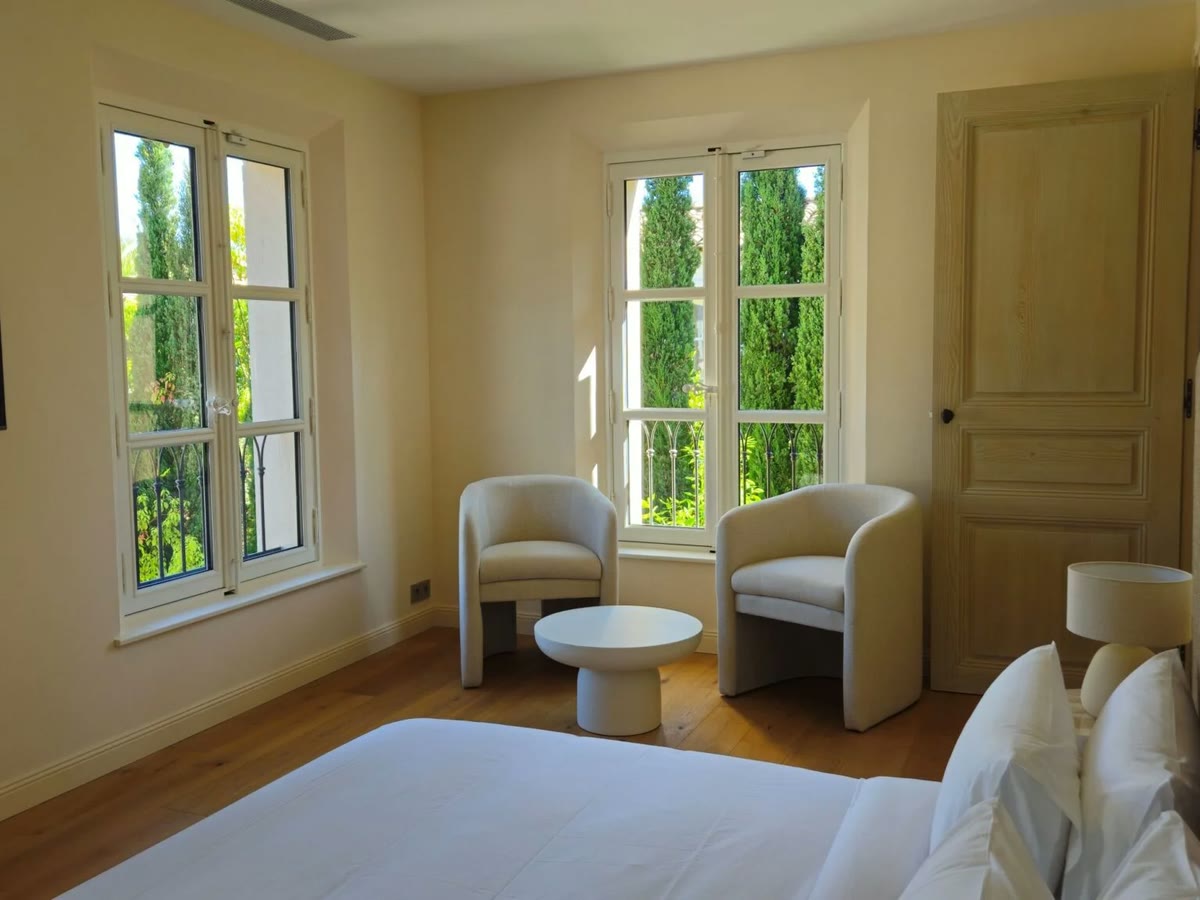 Chambre équipée de fenêtres bois à petits bois ouvertes sur un jardin arboré