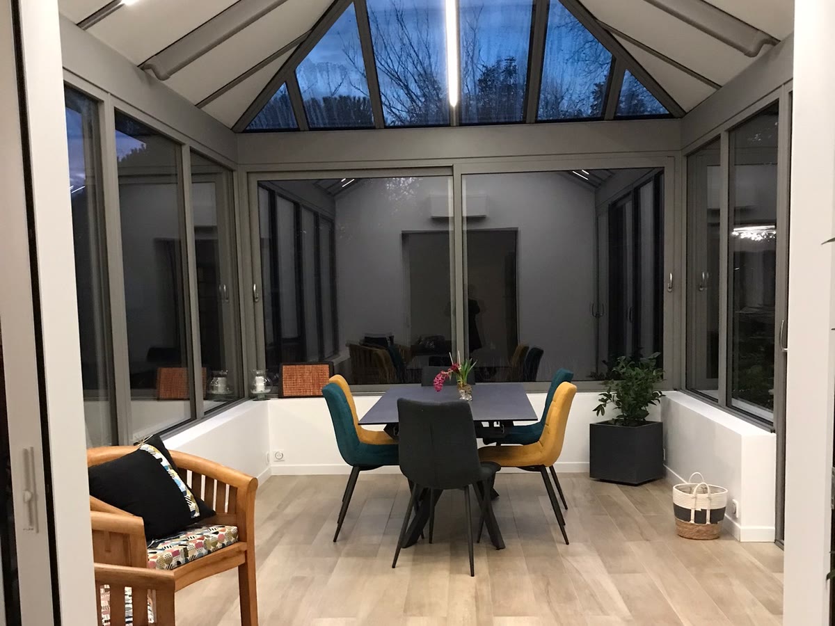Véranda aménagée en salle à manger sous une toiture vitrée